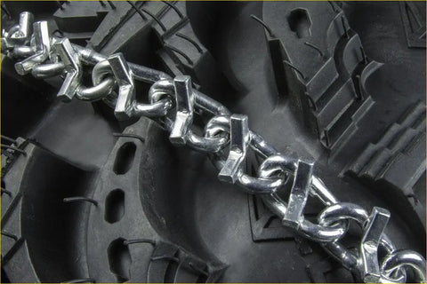 Shiny metallic 2 x raider front tire chains v-bar with interlocking links on rugged black suzuki quadrunner 250 tire