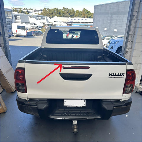 Back view of white toyota hilux with durable textured black tailgate cover featuring black handle and red taillights