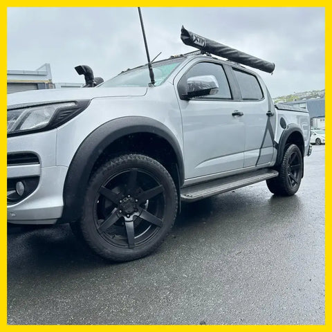 Silver chevrolet colorado with matte black smooth style fender flares black wheels and roof rack carrying kayak