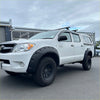 White toyota hilux vigo 2005-2012 with black textured bolt style fender flares and roof rack side view