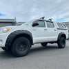 White toyota hilux pickup with black textured bolt style fender flares rugged tires and roof rack