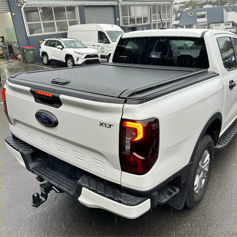 Black retractable manual roller shutter tonneau cover on the back of a white ford ranger xlt 2022+ pickup truck