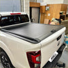 Black manual roll-up tonneau cover on white nissan navara np300 pickup truck back side view