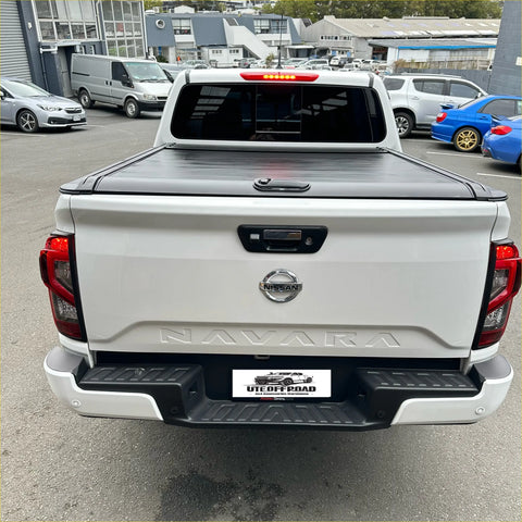 White nissan navara pickup truck with black manual roller shutter tonneau cover shown from the back side