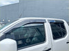 Black plastic window visors installed on white nissan navara d40 pickup showing the front side design