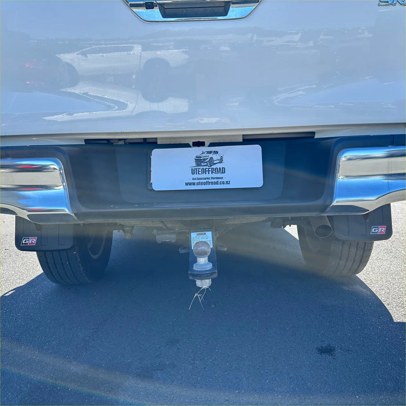 Chrome-finished tow hitch with white plastic cover and safety chain on the back side of matte black mudflaps for toyota hilux 2015+
