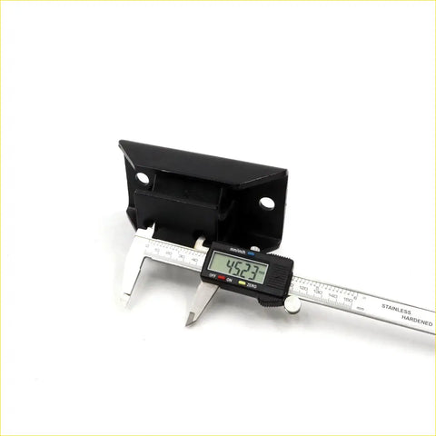 Black plastic rear engine mount bracket for datsun bluebird being measured with digital caliper