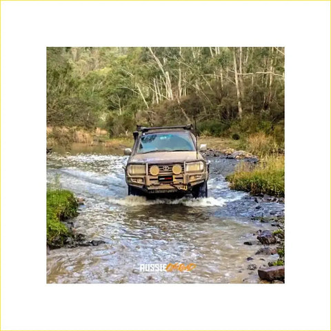 Brown rugged 4wd with rockarmor premium steel bullbar navigating shallow water in forest offroad adventure
