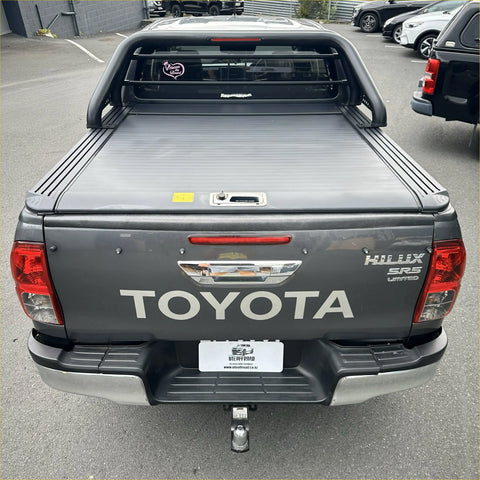 Back view of dark gray toyota hilux srs limited with a ruggedized manual black roller shutter tonneau cover