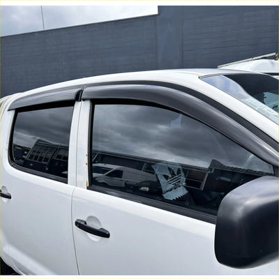 Black plastic window visors installed on a white toyota hilux vigo for weather protection and style