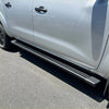 Black metal side step running board along the lower edge of a silver nissan navara 2015-current double cab door