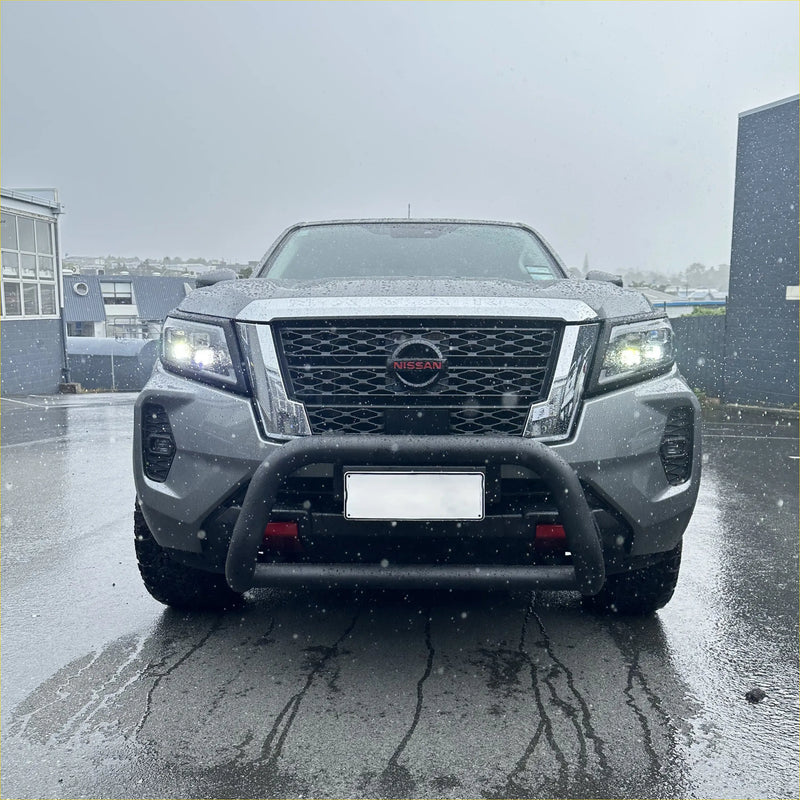 Silver nissan navara pickup with stainless steel black nudge bar and illuminated headlights front view