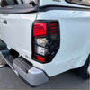 Black plastic taillight covers with red and clear lenses on the back of a white mitsubishi triton 2019-2023 matte black
