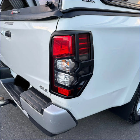 Black plastic taillight covers with red and clear lenses on the back of a white mitsubishi triton 2019-2023 matte black