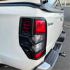 Matte black tail light covers made of black plastic with red and clear lenses on a white 2019-2023 mitsubishi triton
