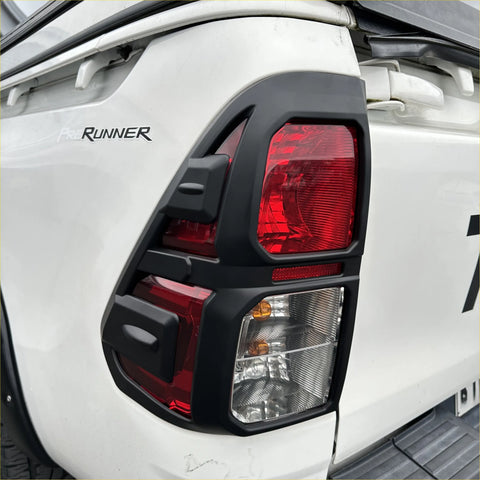 Black plastic taillight cover with red and clear lenses mounted on white toyota hilux 2015-2020 sr sr5 sr5 cruiser